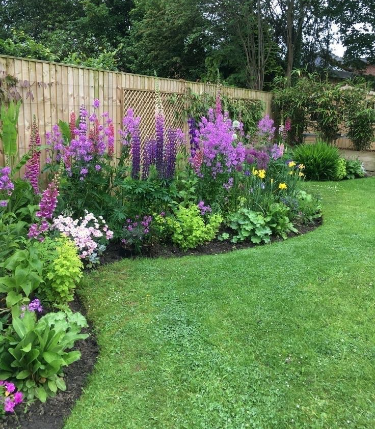 Lush garden bed with vibrant purple and pink flowers, lush green grass, wooden fence.