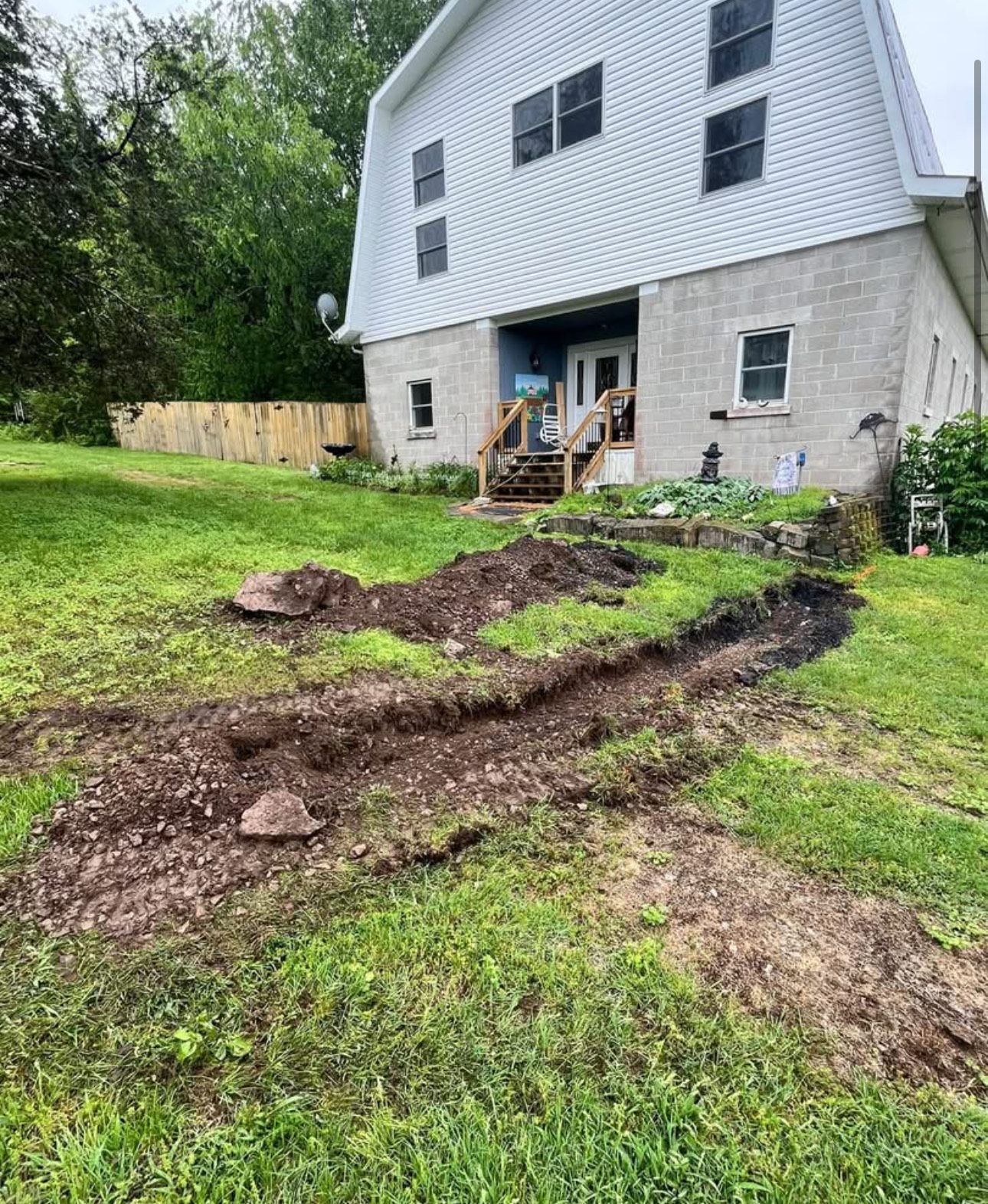 Muddy gravel driveway leading to a home with vehicles parked in the background. Green grass surrounds the drive.