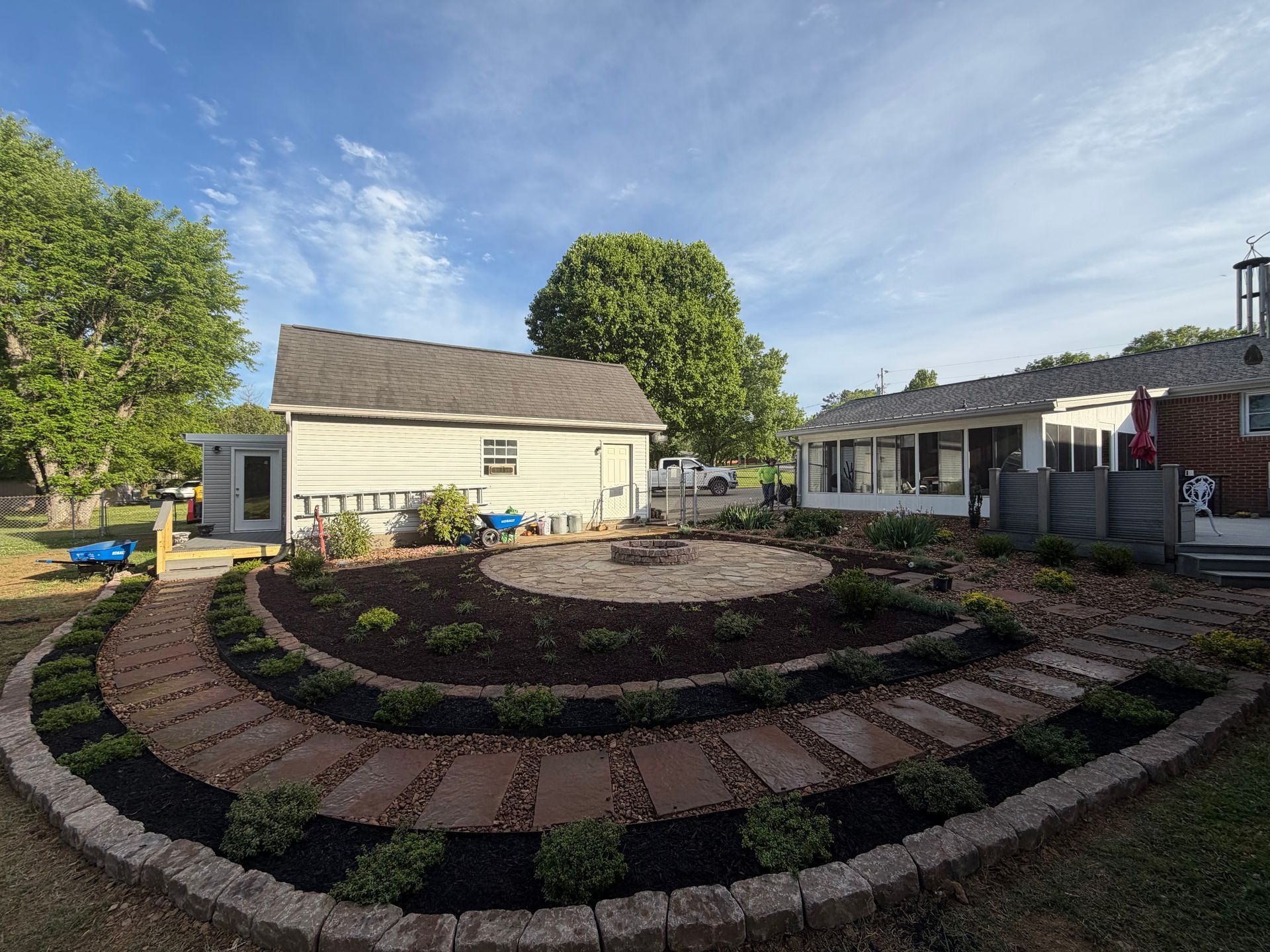 Curved brick garden path around a circular flower bed beside a white house on a sunny day