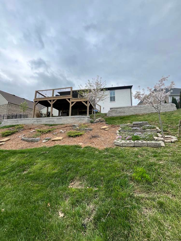 Backyard with a raised deck, terraced landscaping, and a house on a cloudy day. Green grass in the foreground.