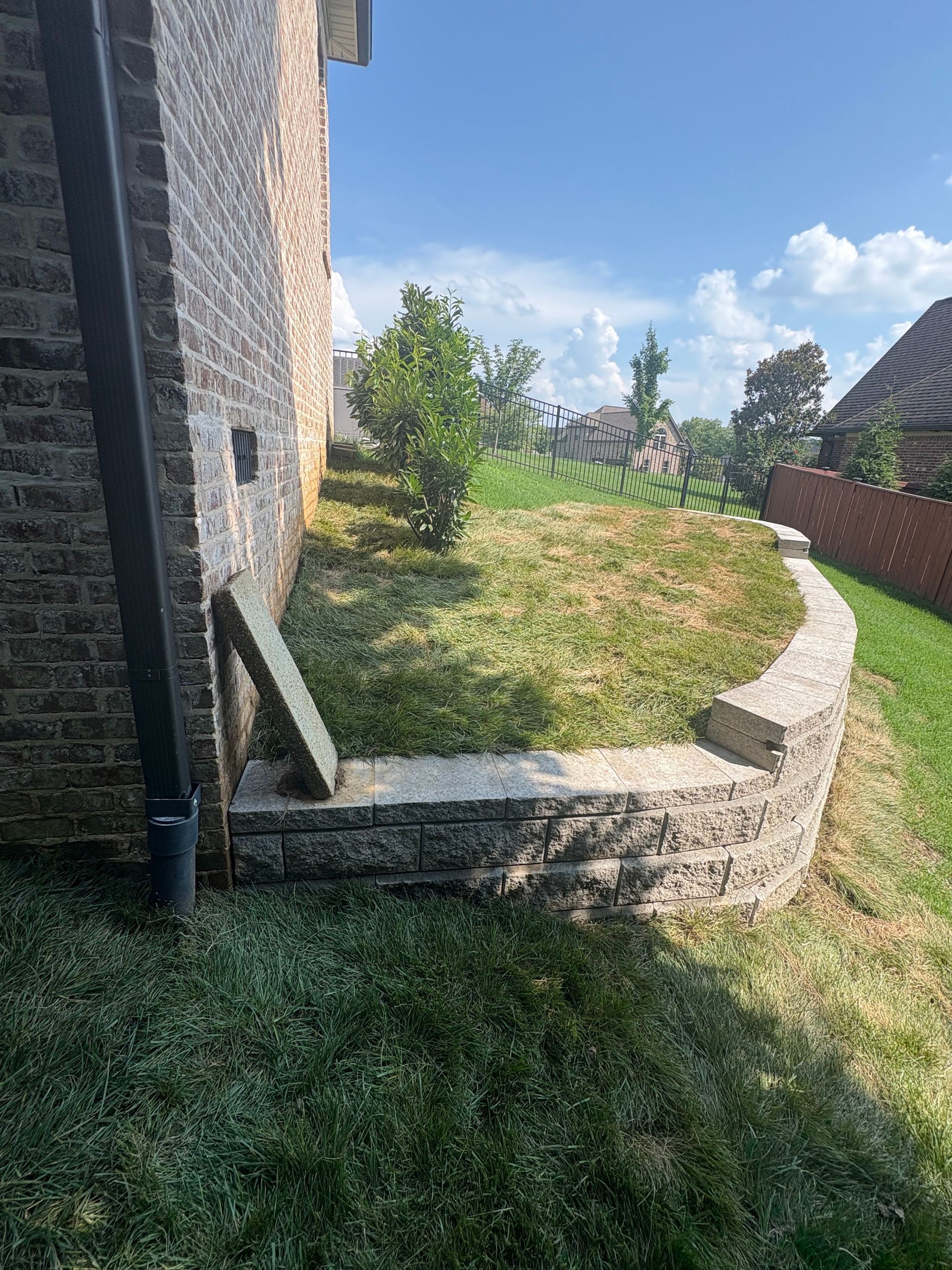 Brick retaining wall in front of a brick building. A grassy area lies behind the wall.