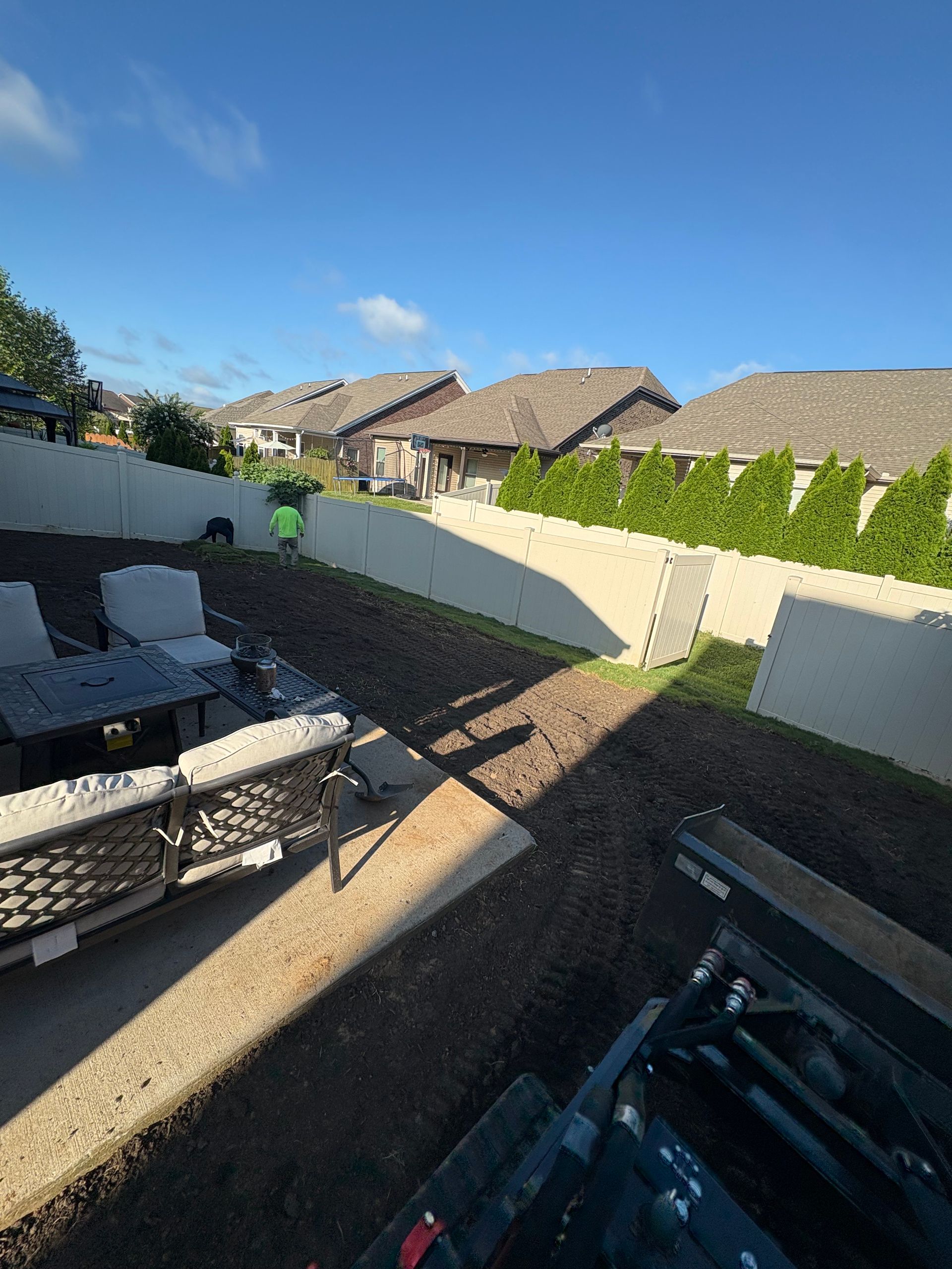 A house with a long, light-colored wall and a vehicle parked on the left. Clear, blue sky.