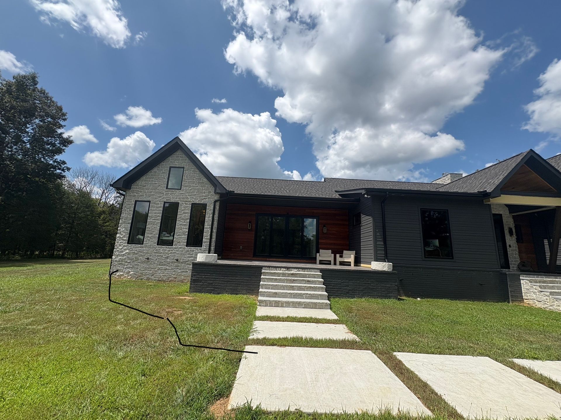 A one-story house on a dirt mound with a detached building. Green grass in the foreground. Overcast sky.