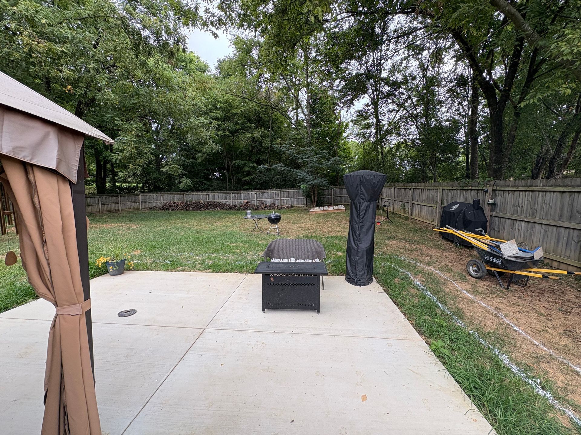 Backyard scene with a patio, fire pit, gazebo, and trees in the background.