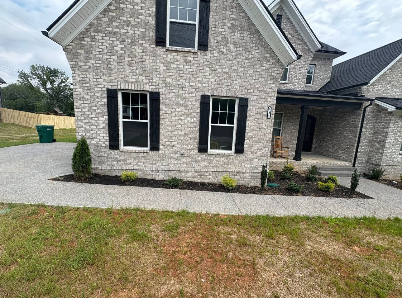 Gray brick house with black shutters and dark roof, on a gravel path.