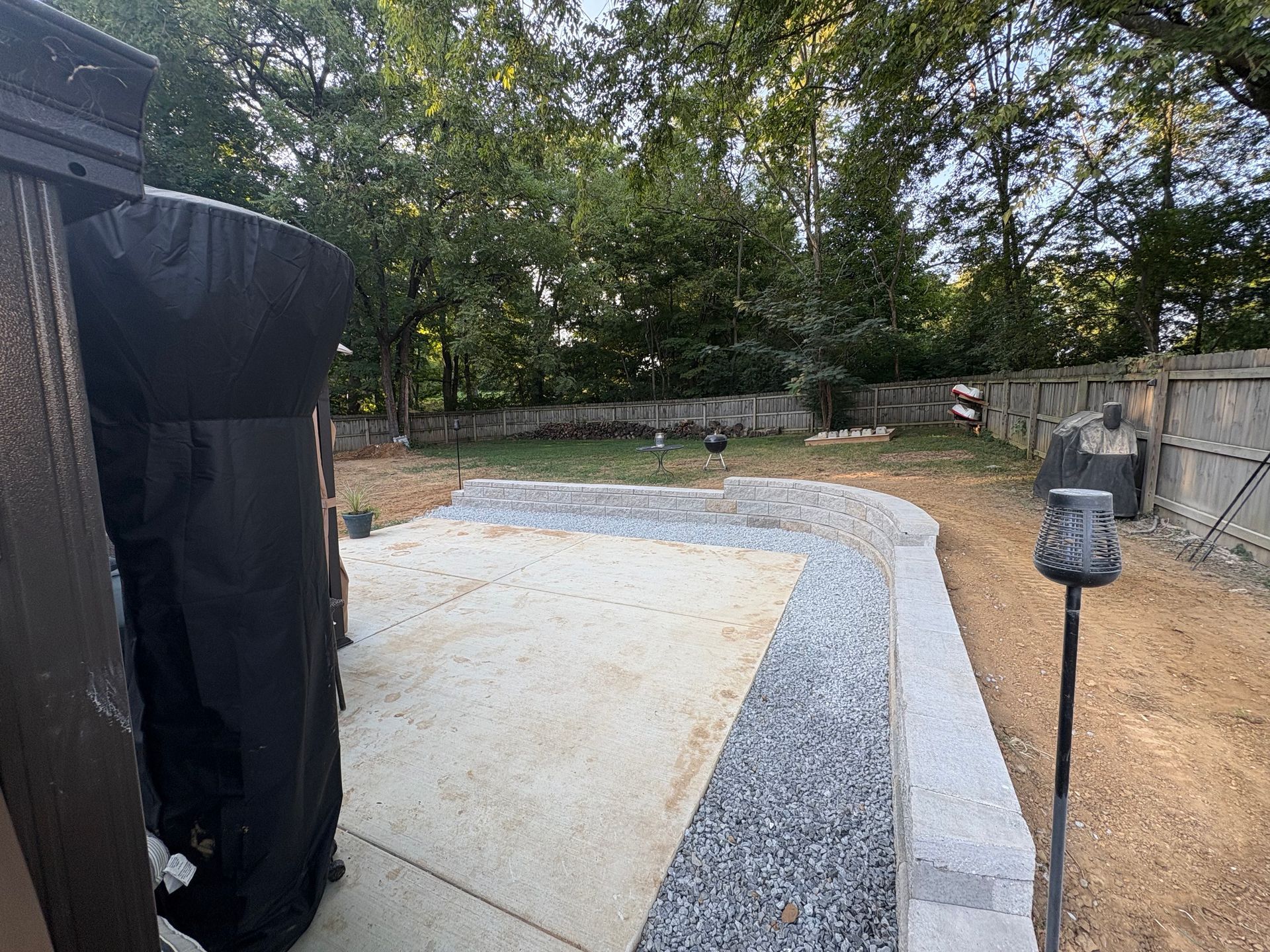 Backyard patio with gravel border, concrete slab, and trees in the background.