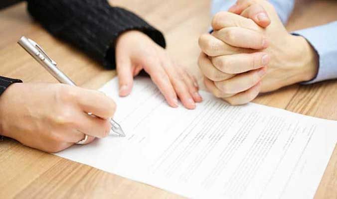 A man and a woman are signing a document on a wooden table.