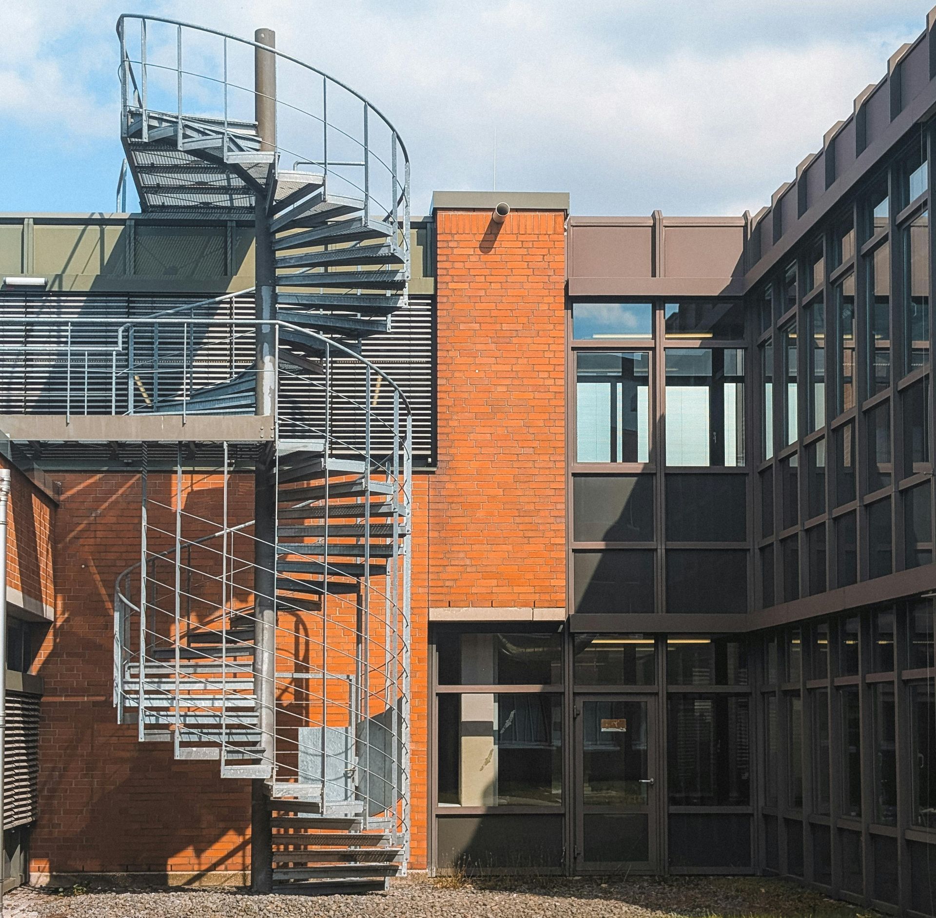 Modern building courtyard with a metal spiral staircase and orange brick and dark glass facades