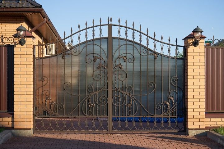 Ornate black wrought-iron gate between brick pillars and brick walls at a driveway entrance