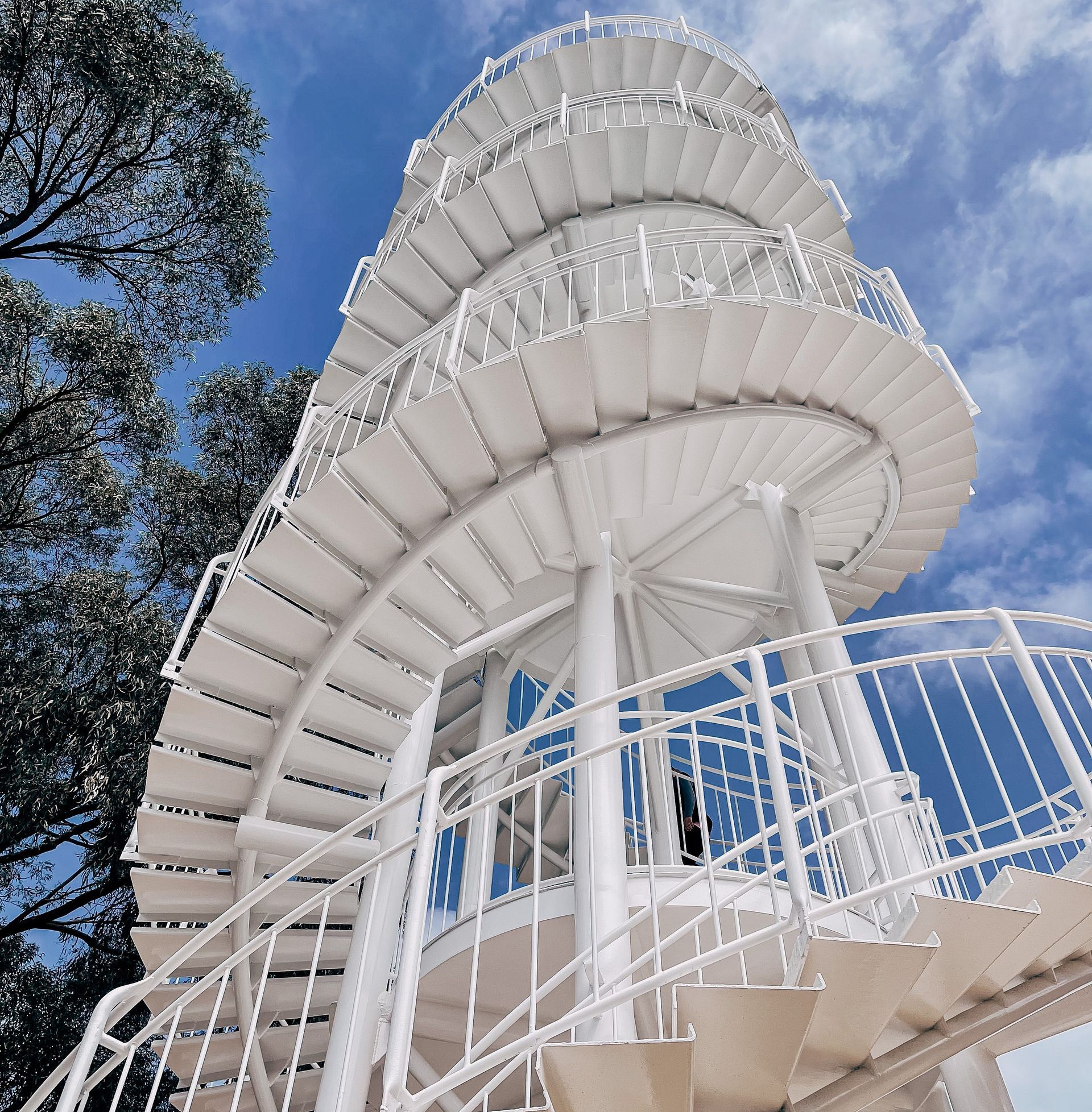 White spiral staircase and railing against a bright blue sky with clouds