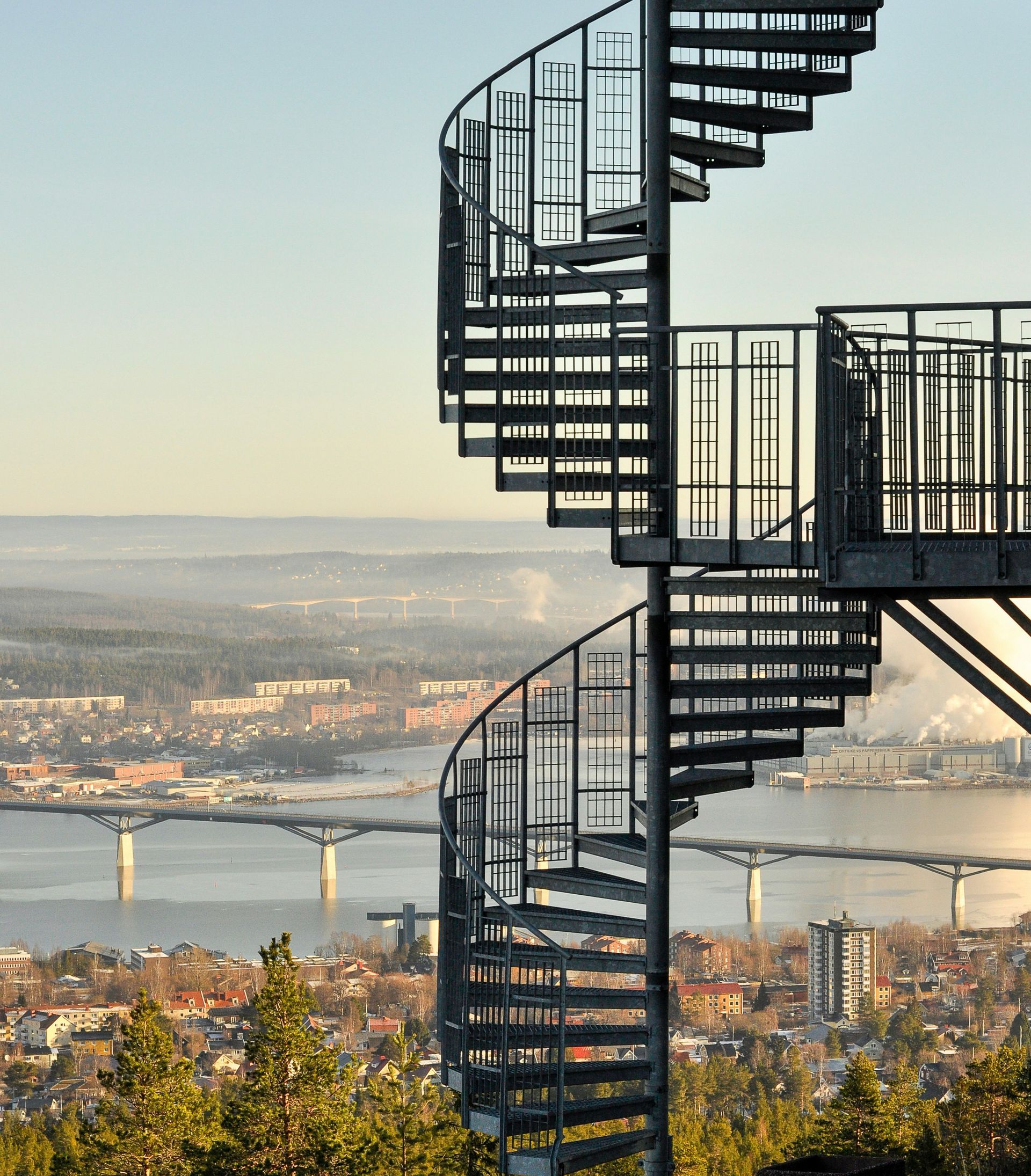 Curving metal spiral staircase on a hill overlooking a river and Atherton city skyline at sunset