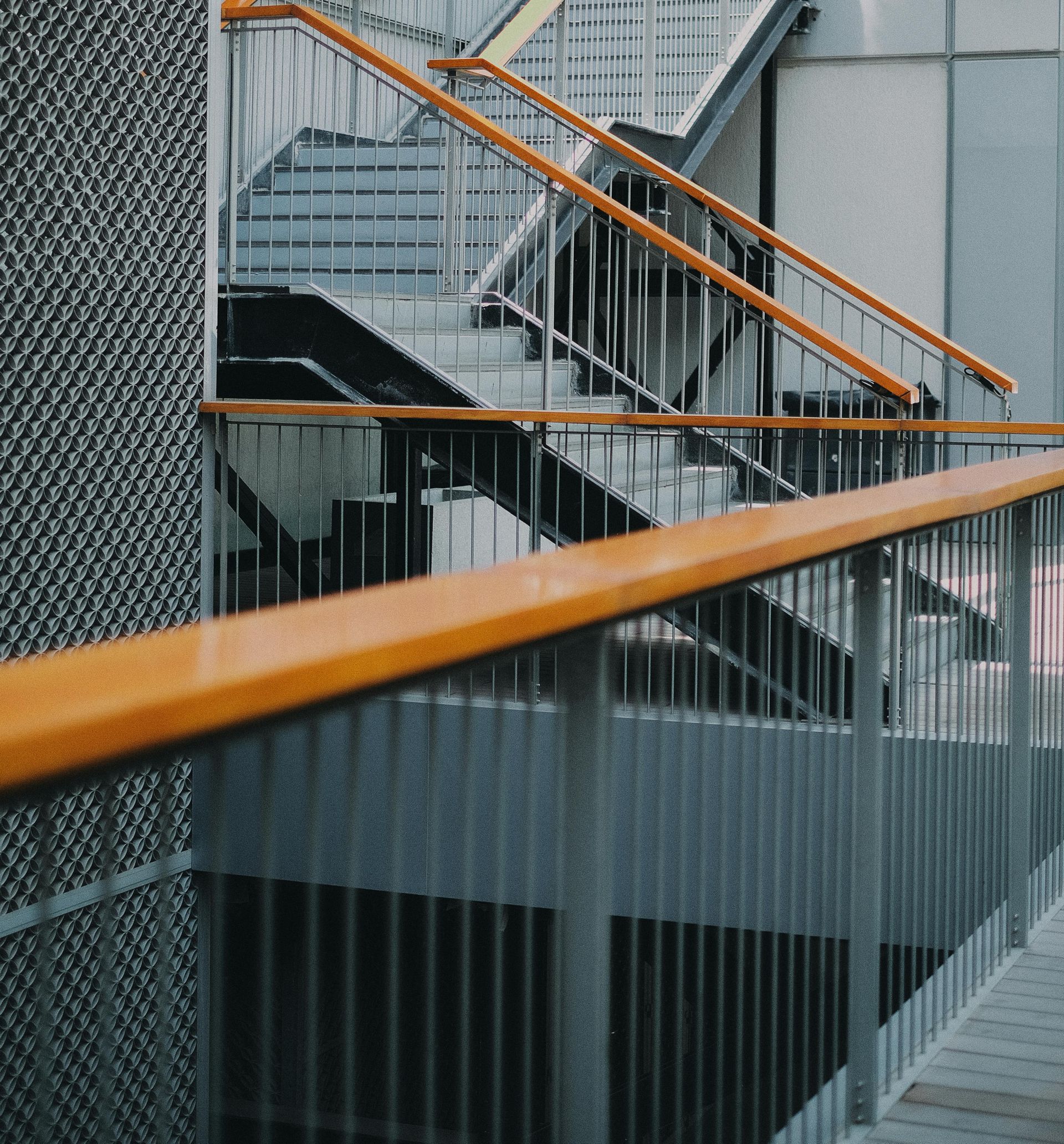Modern stairway with orange handrails and a black lattice wall in a gray industrial interior