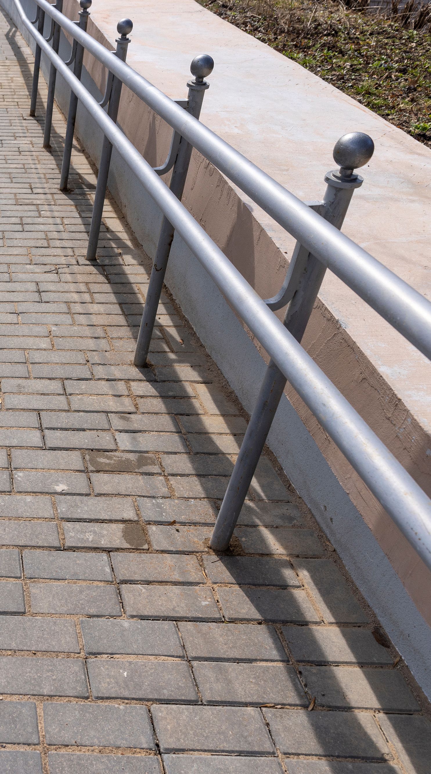 Metal railing with spherical tops along sunlit brick path