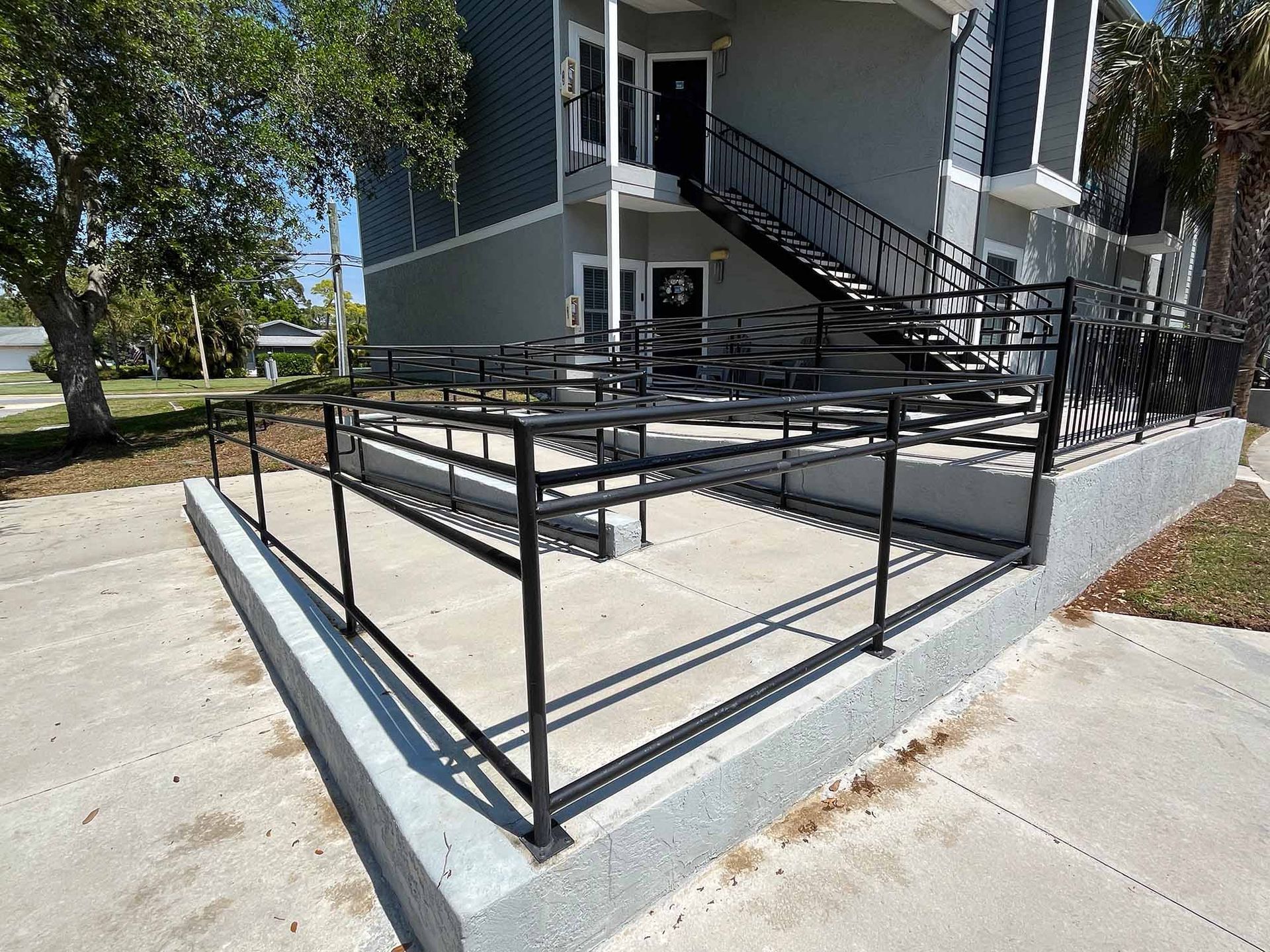 A gray metal external staircase and balcony attached to a beige building with multiple doors and windows.
