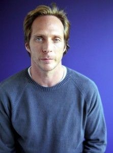 A man in a blue sweater is standing in front of a blue wall.