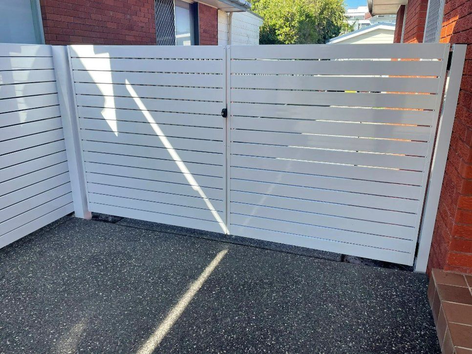 A White Fence Is Sitting in Front of A Brick Building — Topline Aluminium Forster Pty Ltd in Hallidays Point, NSW