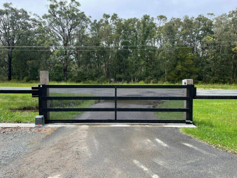 A Black Gate Is Sitting on The Side of A Road Next to A Grassy Field — Topline Aluminium Forster Pty Ltd in Forster, NSW