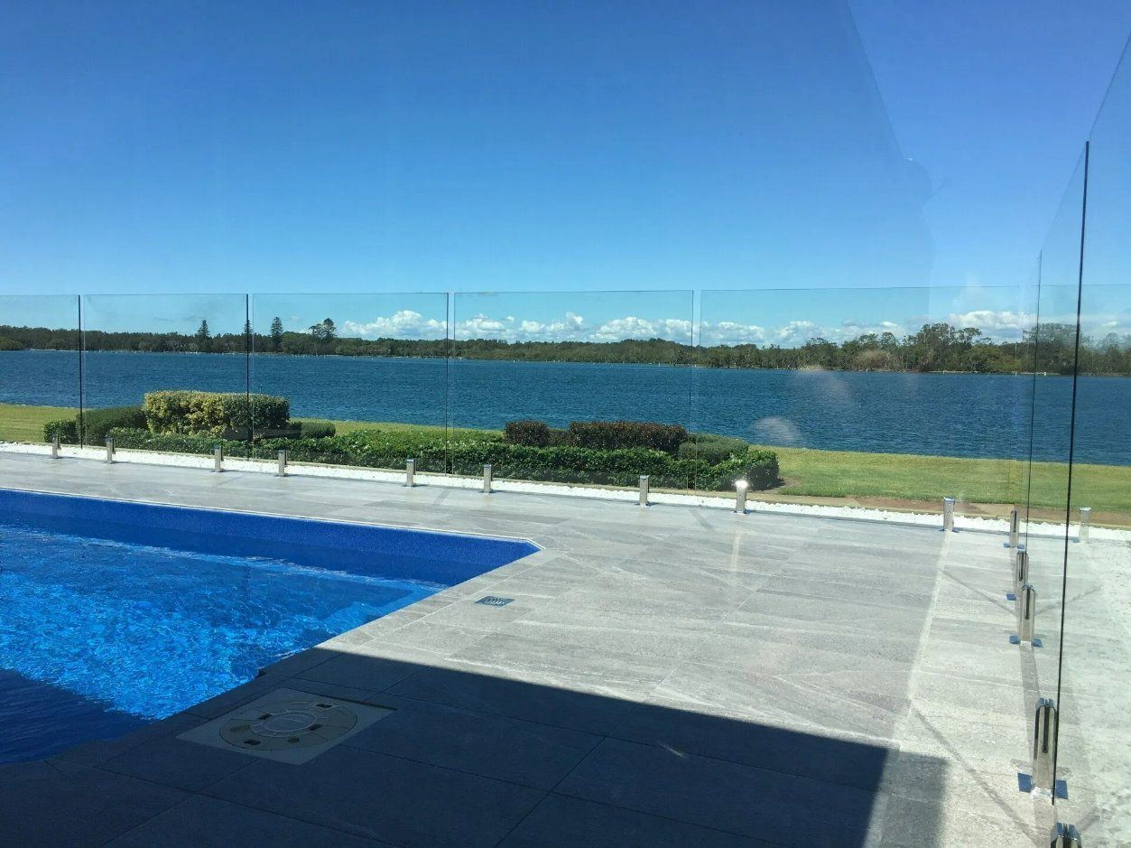 A Swimming Pool with A Glass Fence and A View of A Lake — Topline Aluminium Forster Pty Ltd in Hallidays Point, NSW