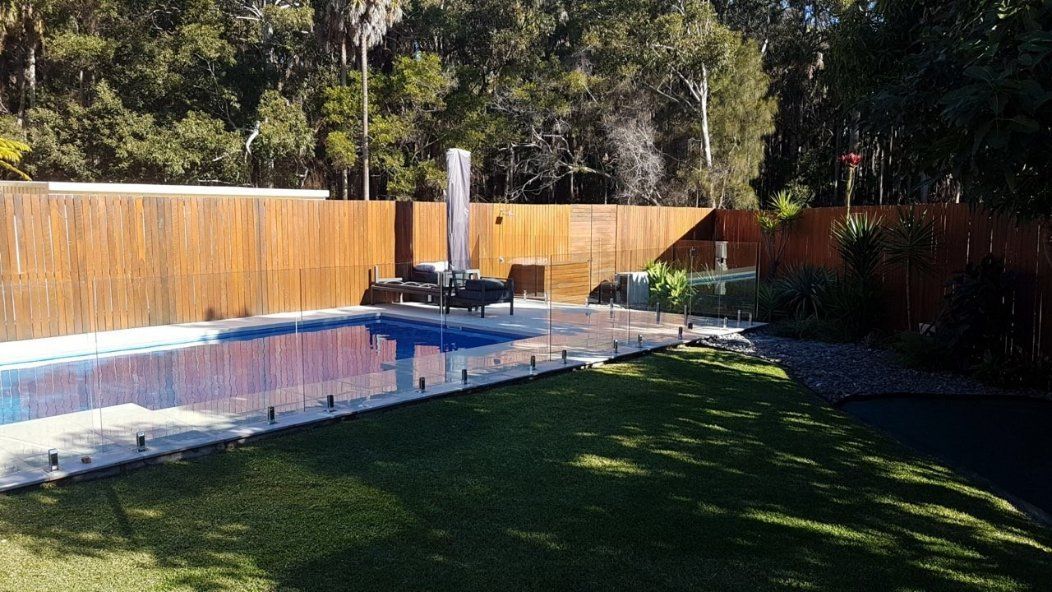 A Large Swimming Pool Is Surrounded by A Wooden Fence in A Backyard — Topline Aluminium Forster Pty Ltd in Harrington, NSW