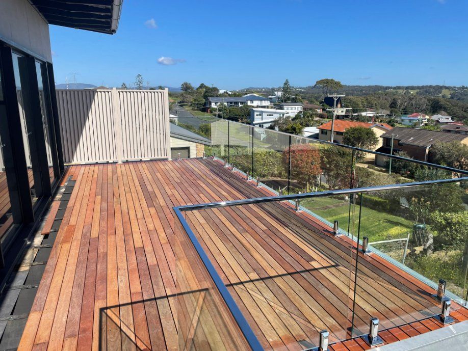A Wooden Deck with A Glass Railing and A View of A City — Topline Aluminium Forster Pty Ltd in Forster, NSW