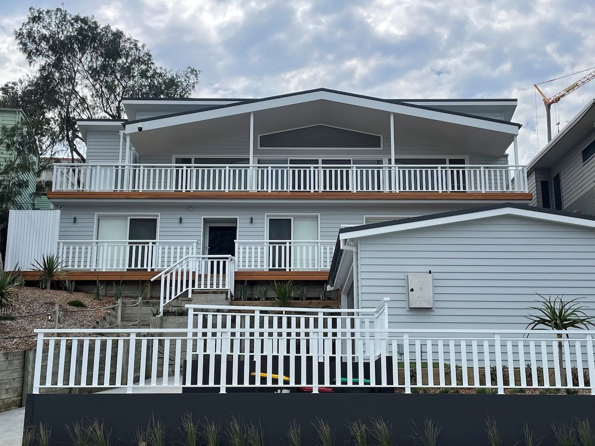 A White House with A Striped Awning on The Balcony — Topline Aluminium Forster Pty Ltd in Forster, NSW
