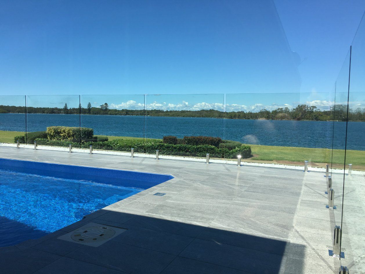 A Swimming Pool with A View of A Lake Behind a Glass Fence — Topline Aluminium Forster Pty Ltd in Taree, NSW
