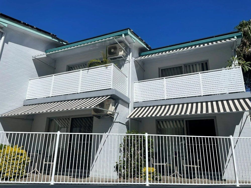 A White House with A Striped Awning on The Balcony — Topline Aluminium Forster Pty Ltd in Hallidays Point, NSW