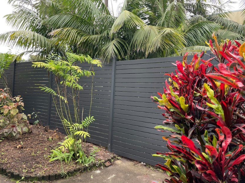 A black fence surrounds a garden with lots of plants and palm trees. — Topline Aluminium Forster Pty Ltd in Smiths Lake, NSW