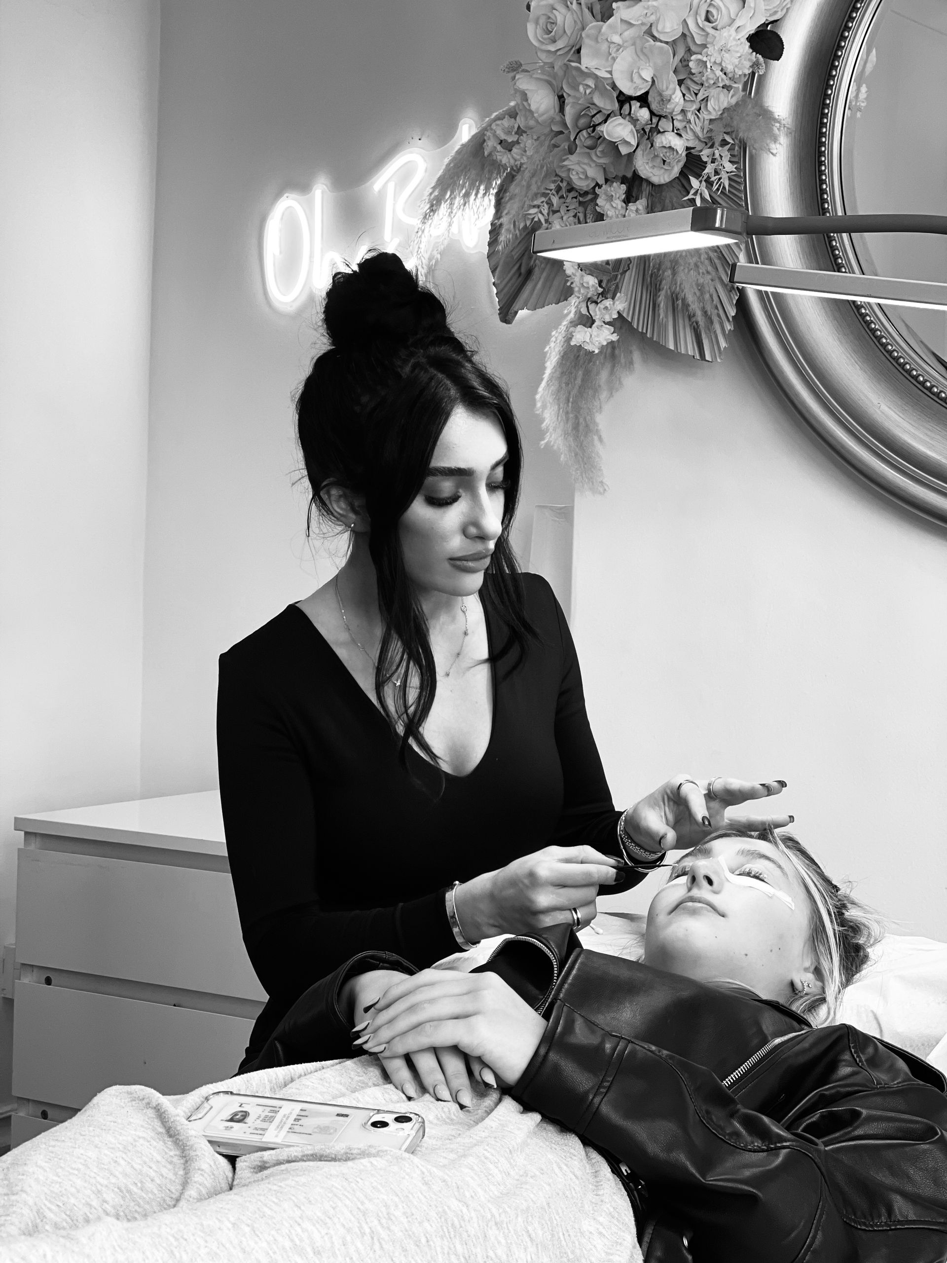 Anya Ely is applying eyelash extensions to a woman laying on a bed .