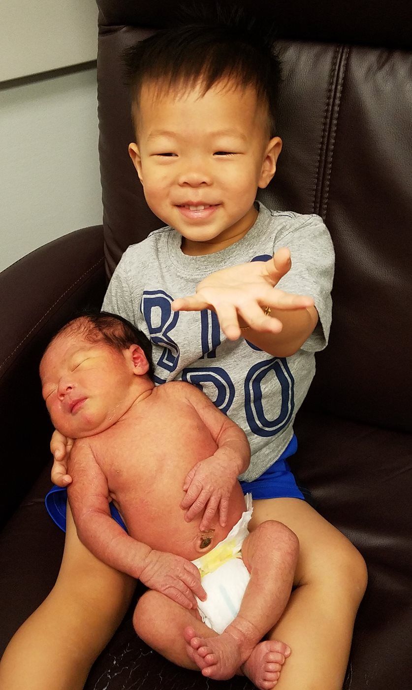 A young boy is holding a newborn baby in his arms.