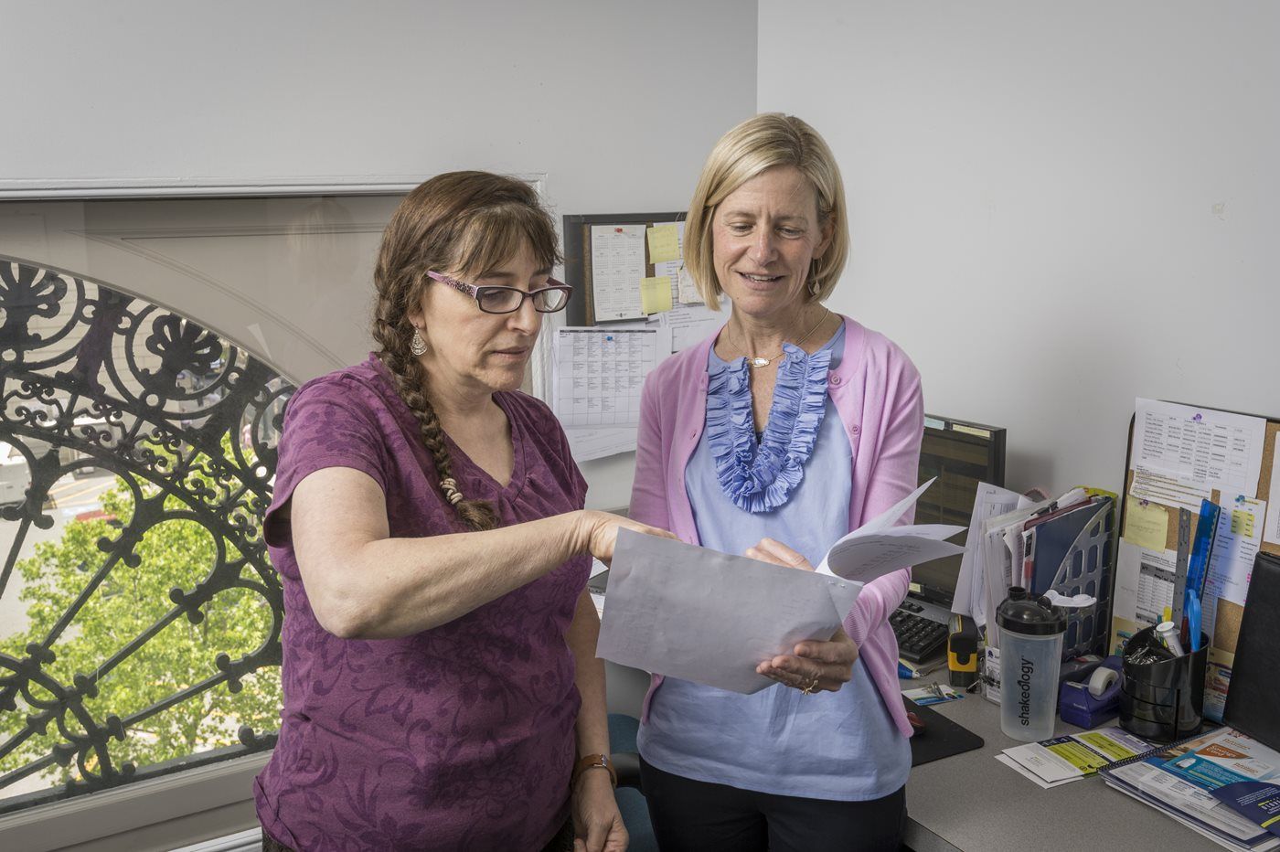 Two women are standing next to each other in an office looking at a piece of paper.