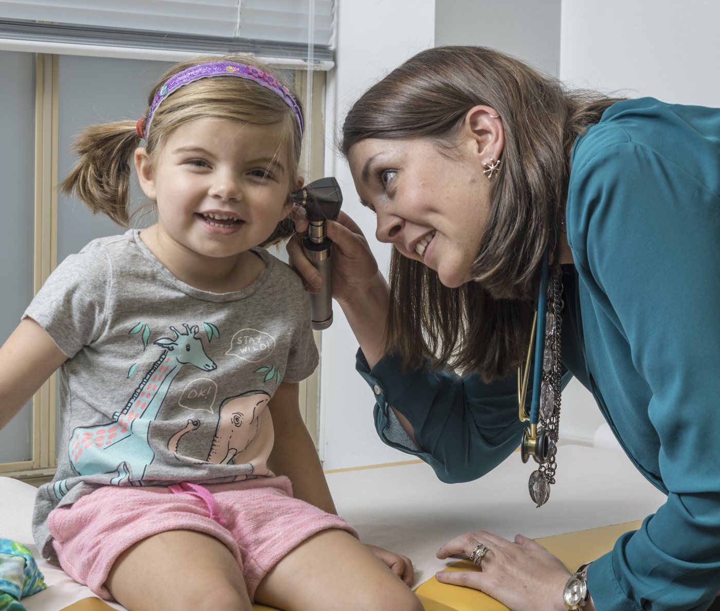 A pediatrician is looking into a little girl's ear with a magnifying glass.
