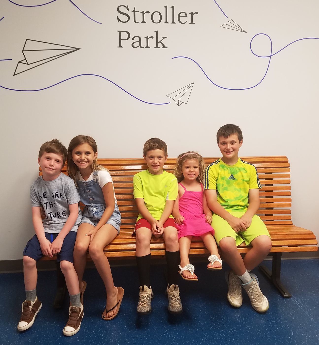 Five children sit on a wooden bench at