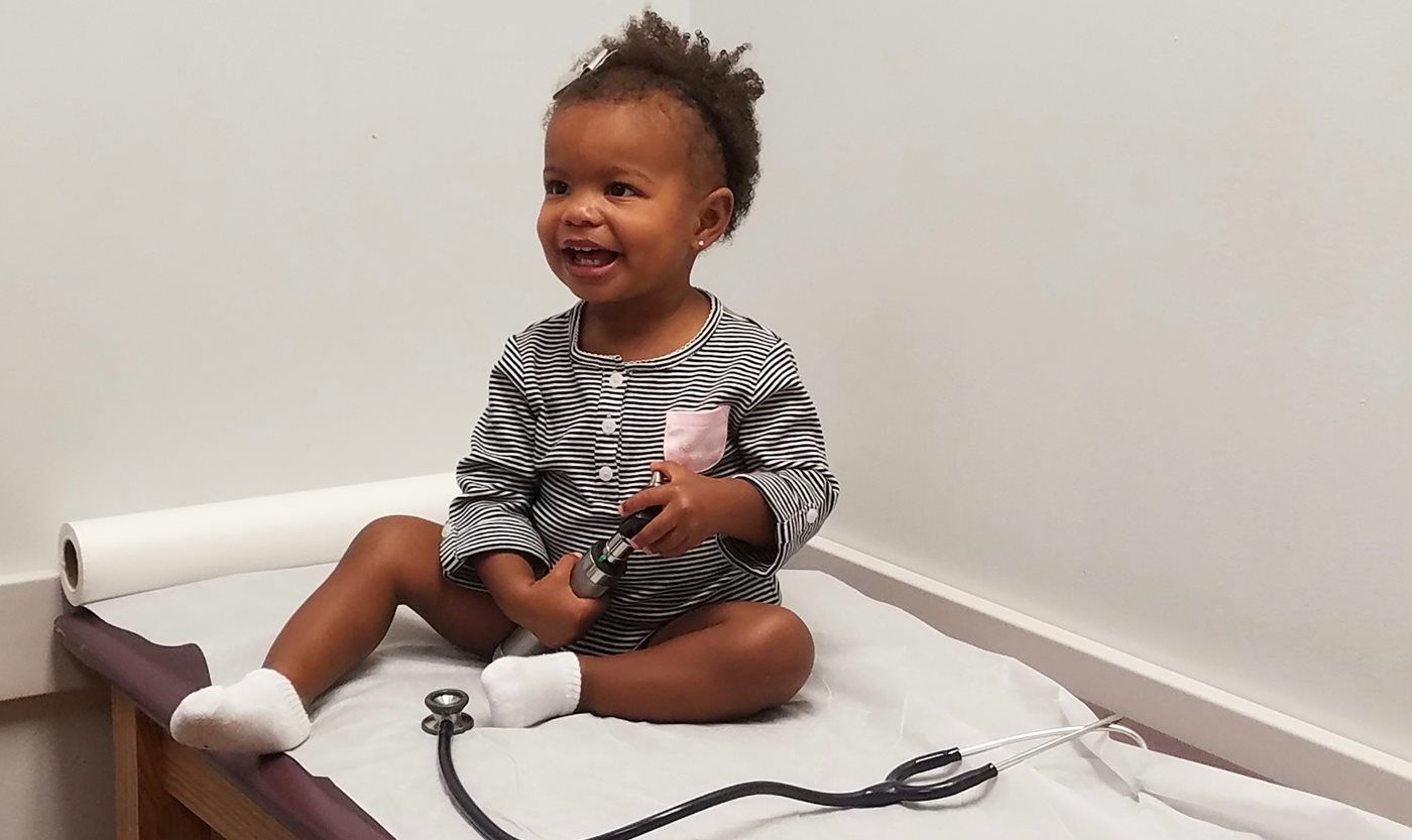A little girl is sitting on a table with a stethoscope.