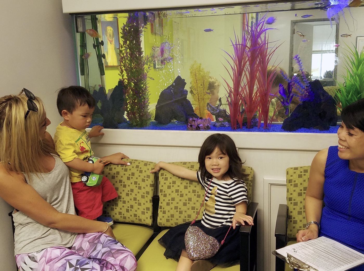 Two women and two children are sitting in a waiting room in front of an aquarium.