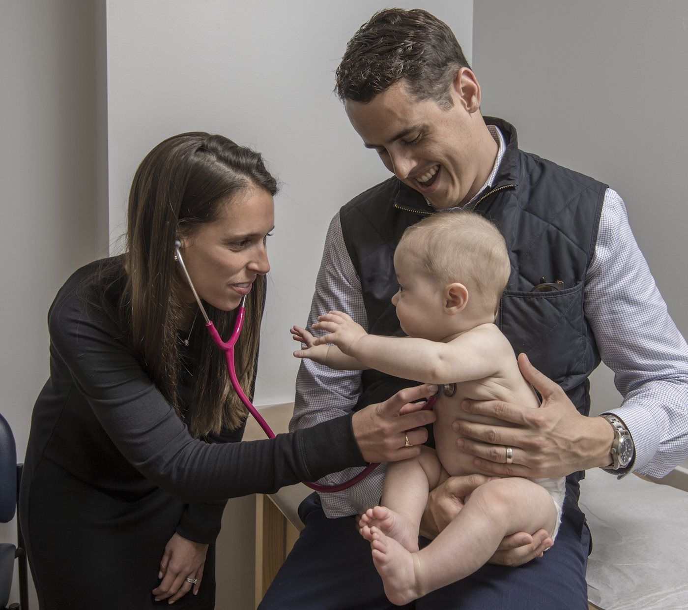 A man and a woman are examining a baby with a stethoscope.