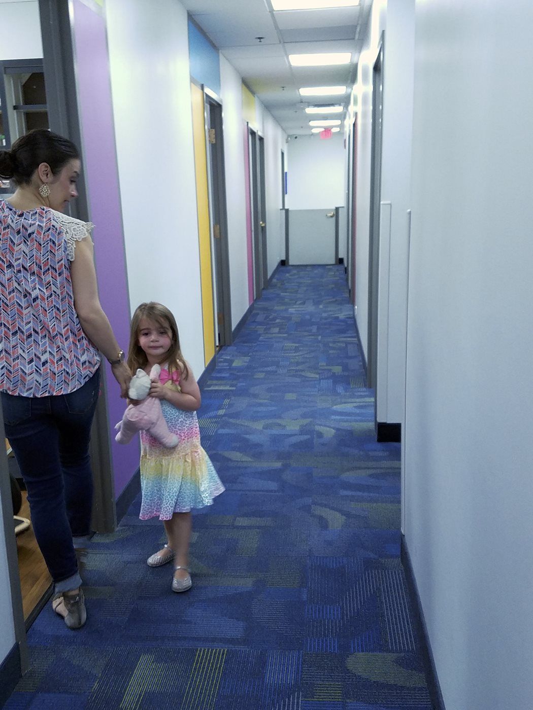 A woman and a little girl are walking down a hallway.
