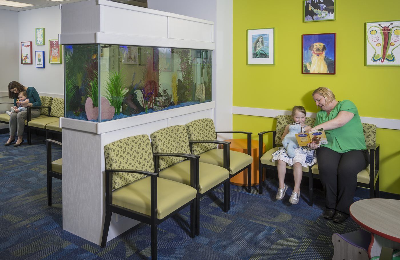 A woman is reading a book to a little girl in a waiting room.