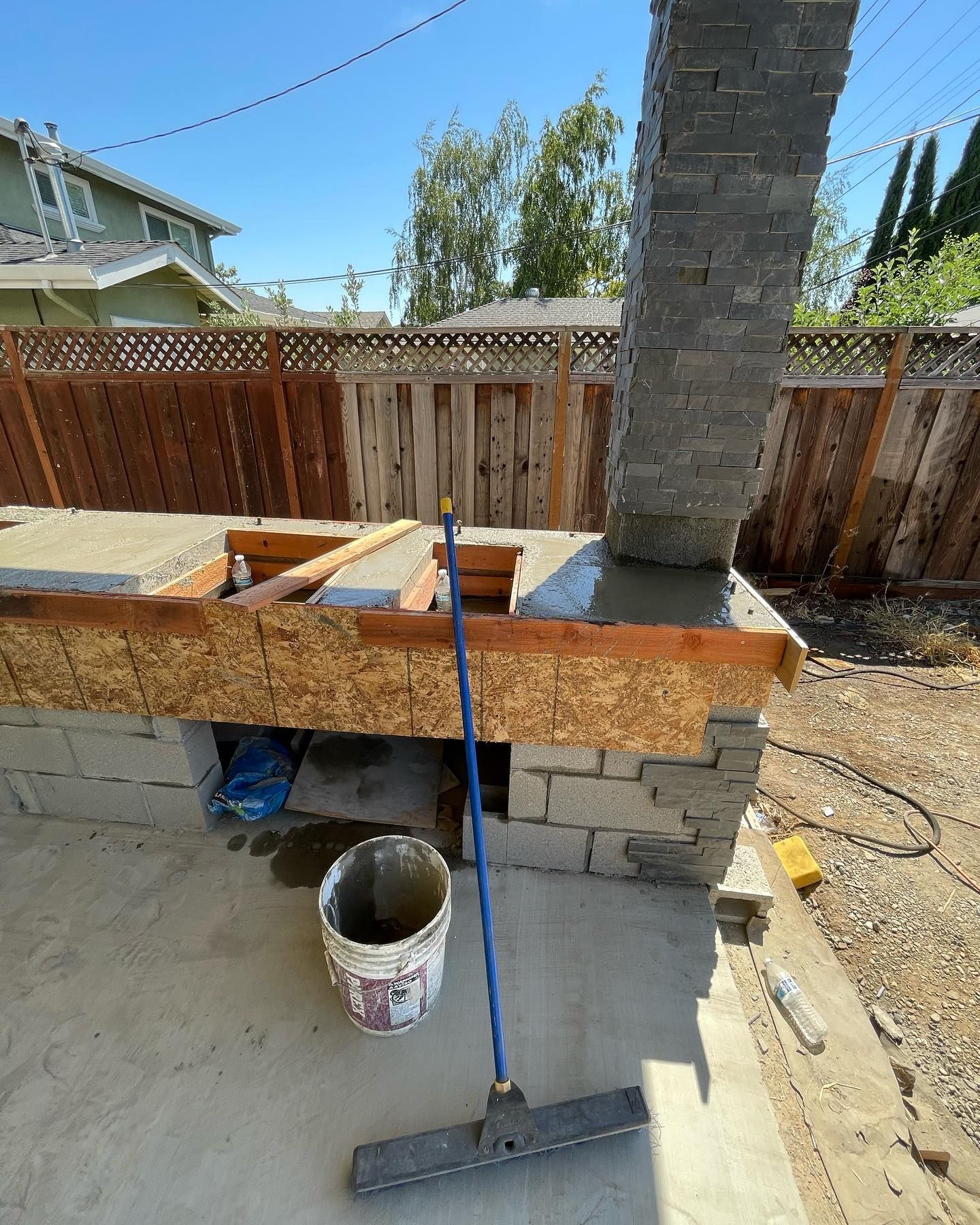 A broom is sitting on the ground next to a bucket of cement.