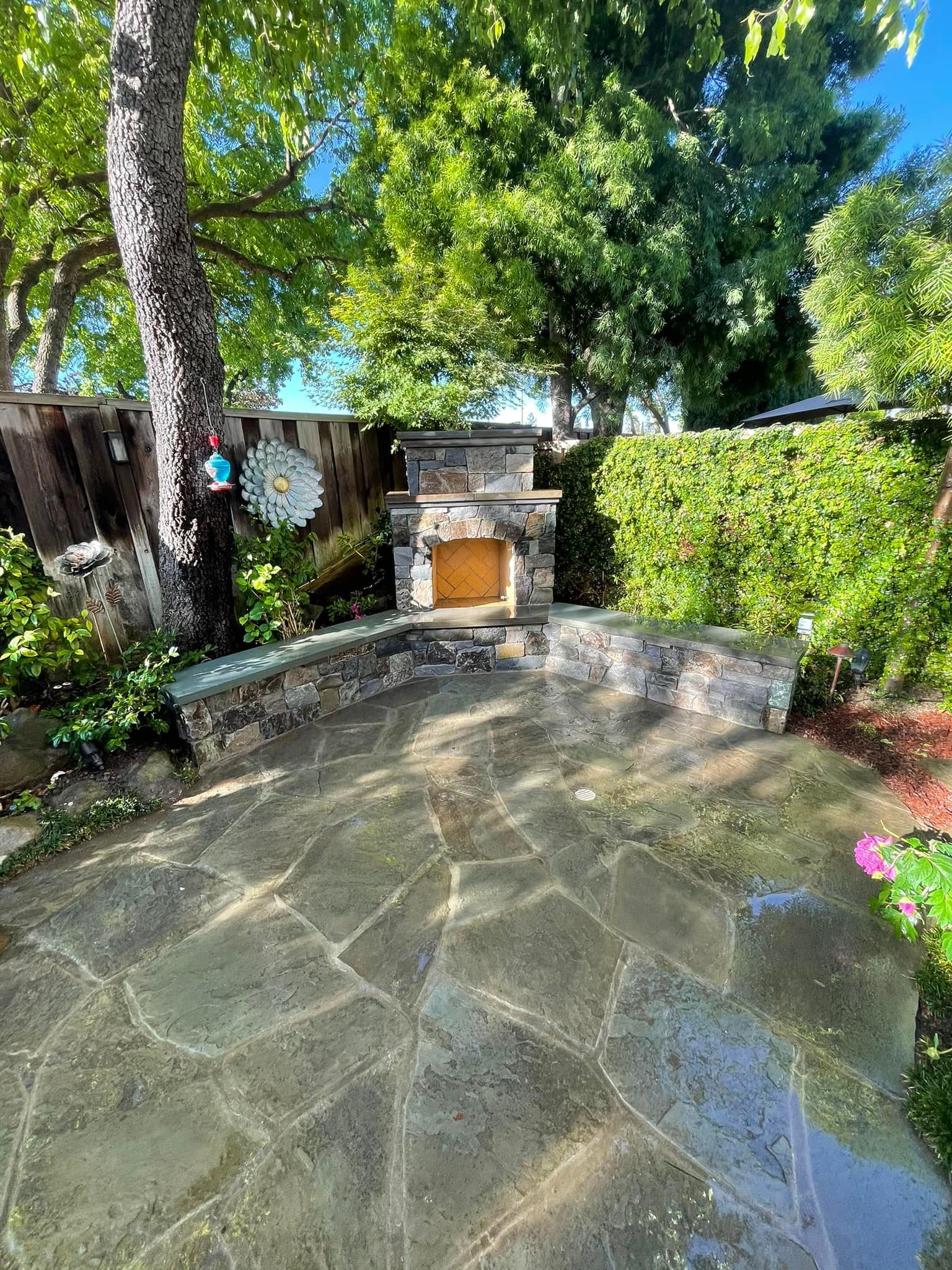 A stone patio with a fireplace in the backyard.