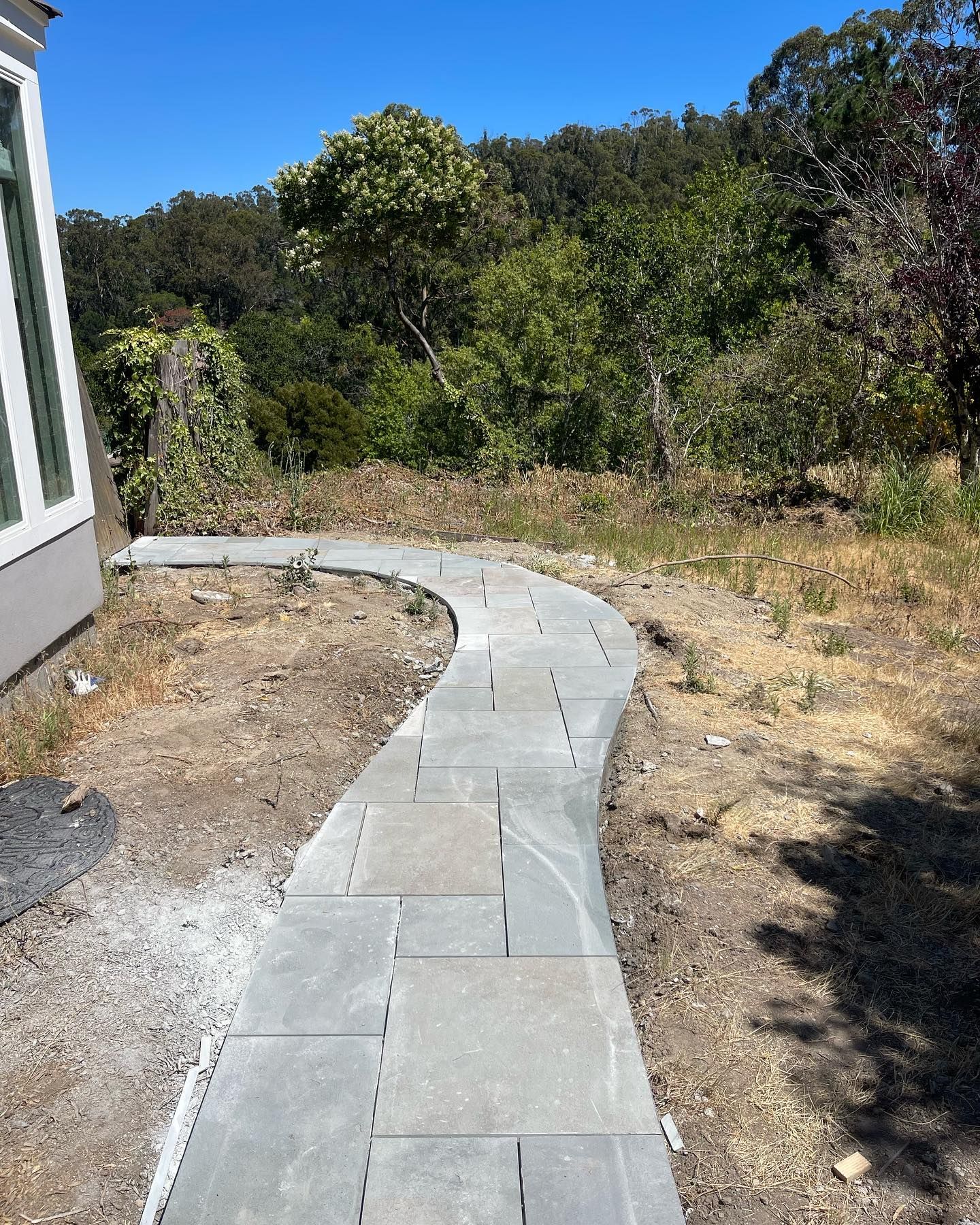 A curved walkway leading to a house with trees in the background.