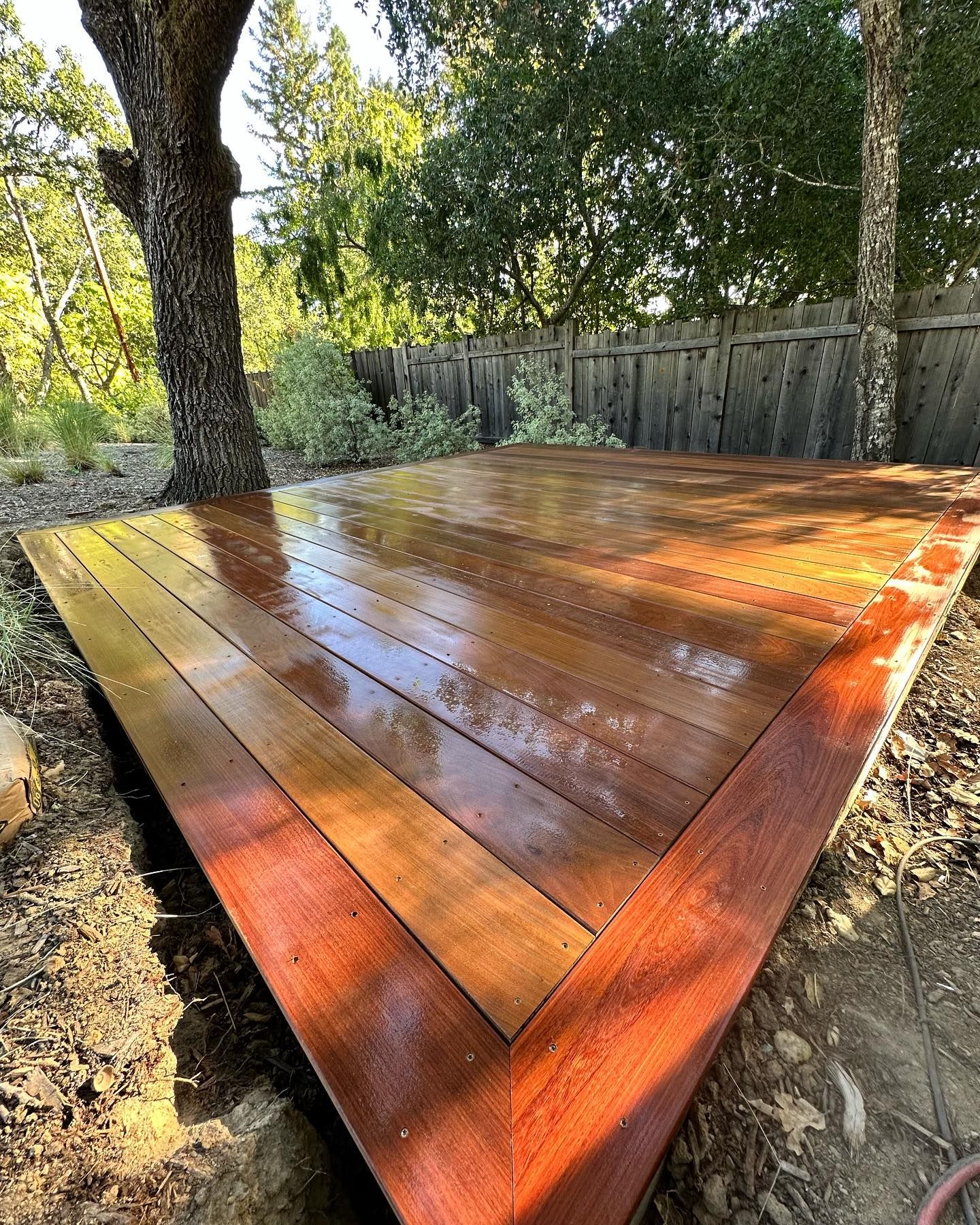 A wooden deck with a tree in the background and a fence in the background.