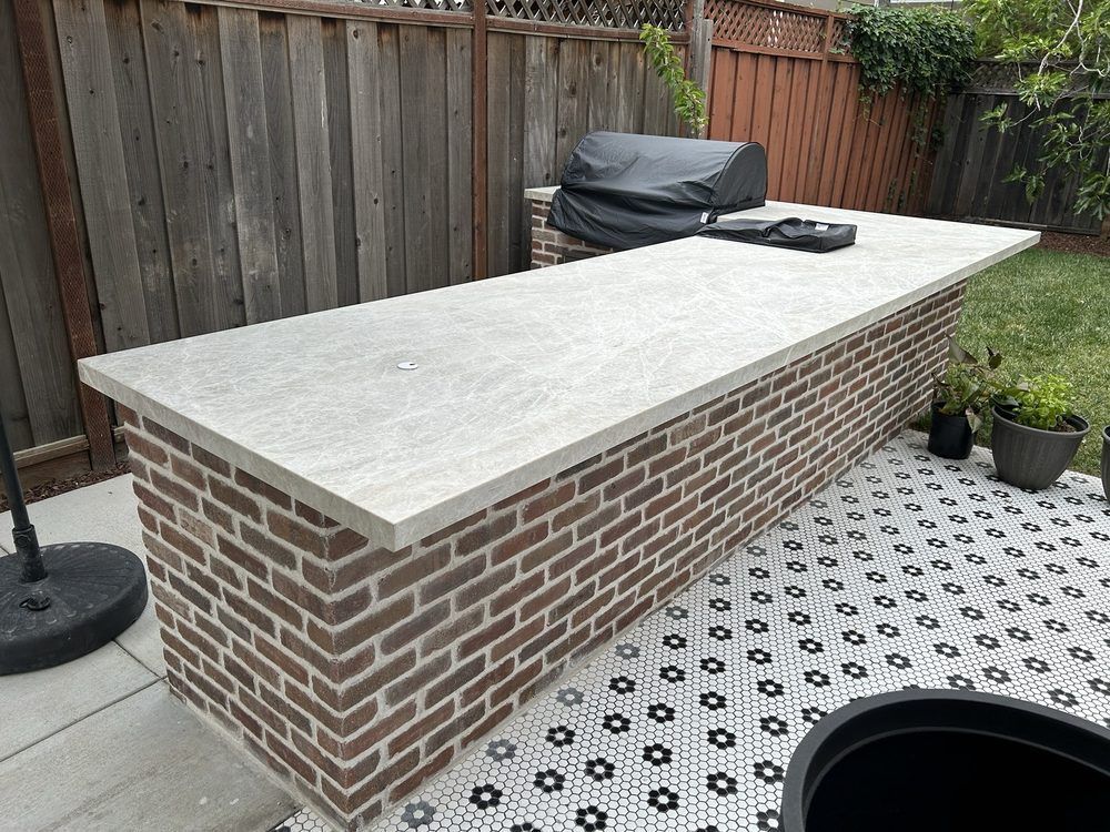 A large brick table with a concrete top is sitting on a patio next to a grill.