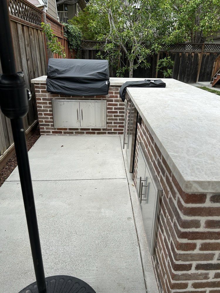 A grill is sitting on top of a brick counter in a backyard.