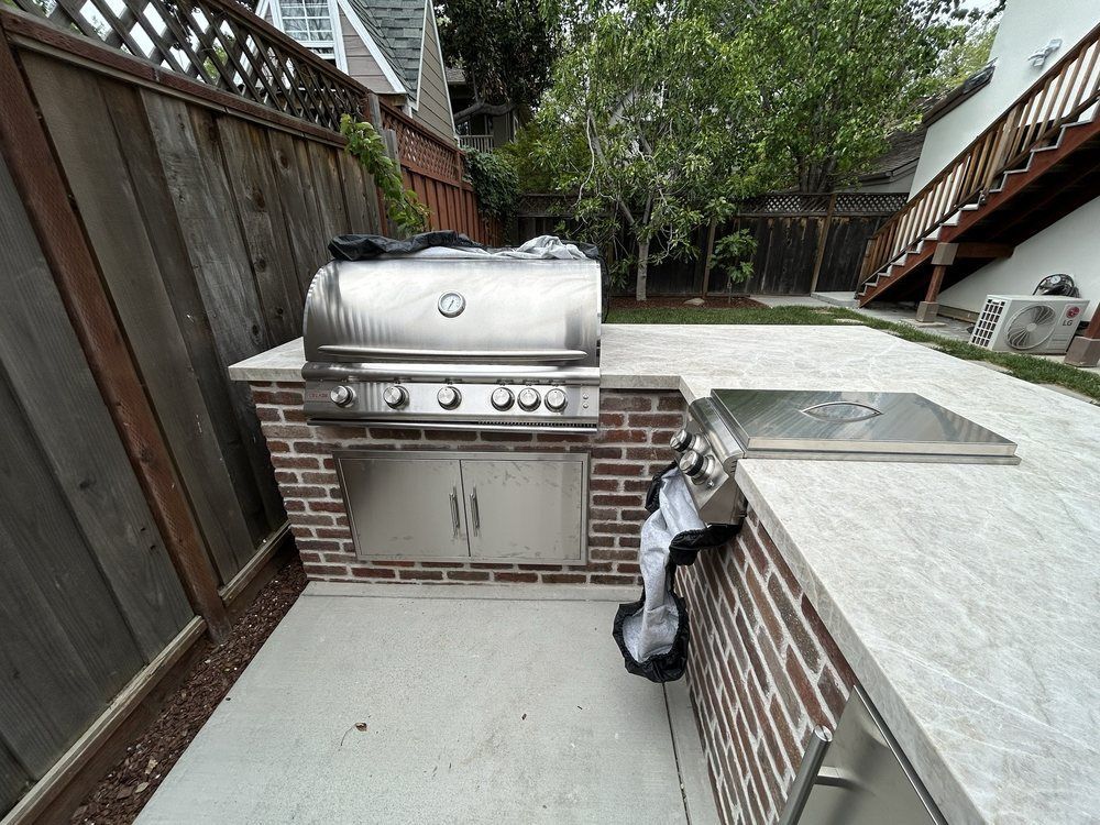 A grill is sitting on top of a brick counter in a backyard.