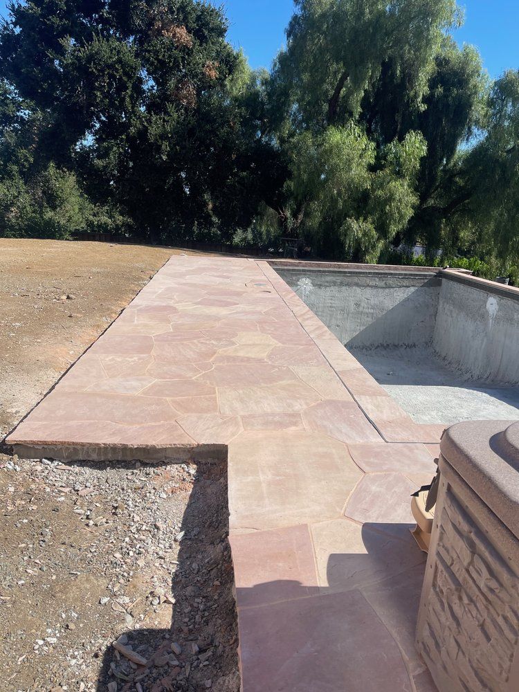 A concrete walkway leading to a swimming pool with trees in the background.