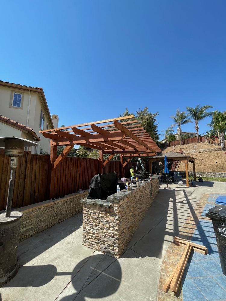 A wooden pergola is being built over a stone island in a backyard.