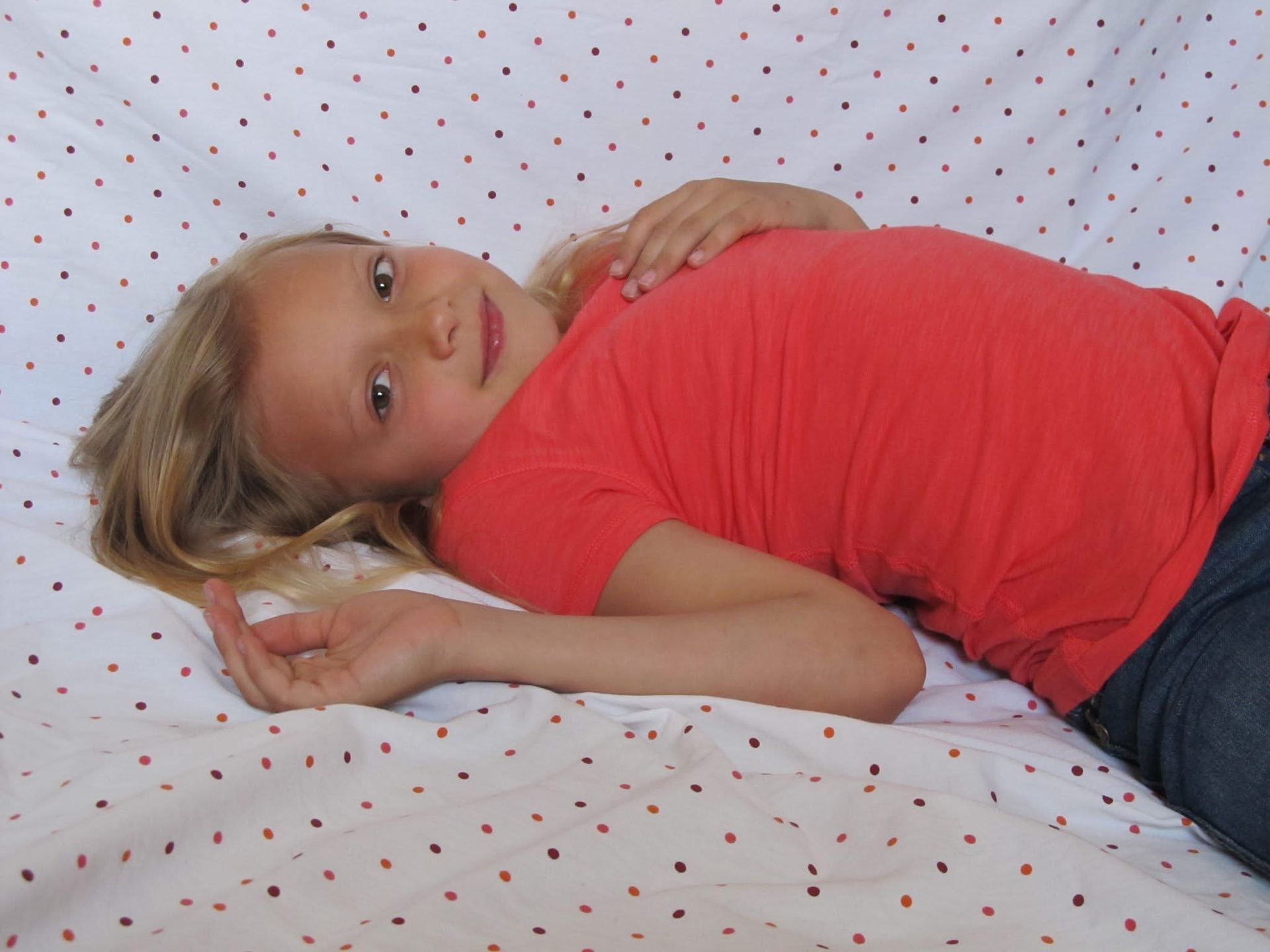 A person in a red shirt and jeans lying on a white surface with small red and black polka dots.