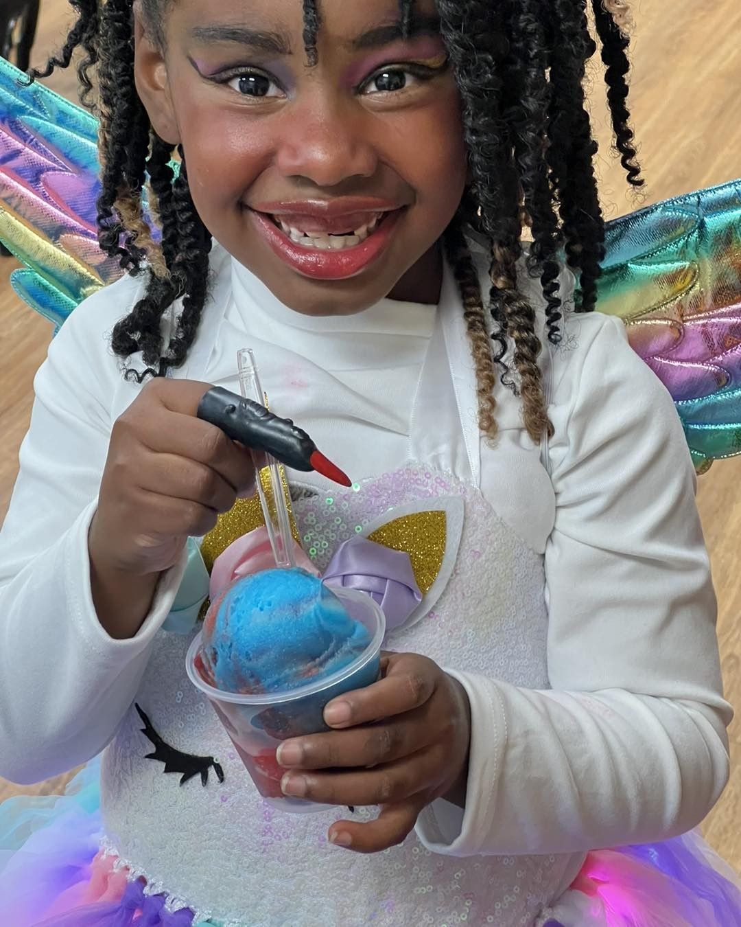 Girl in unicorn costume smiling, holding a colorful drink and marker.