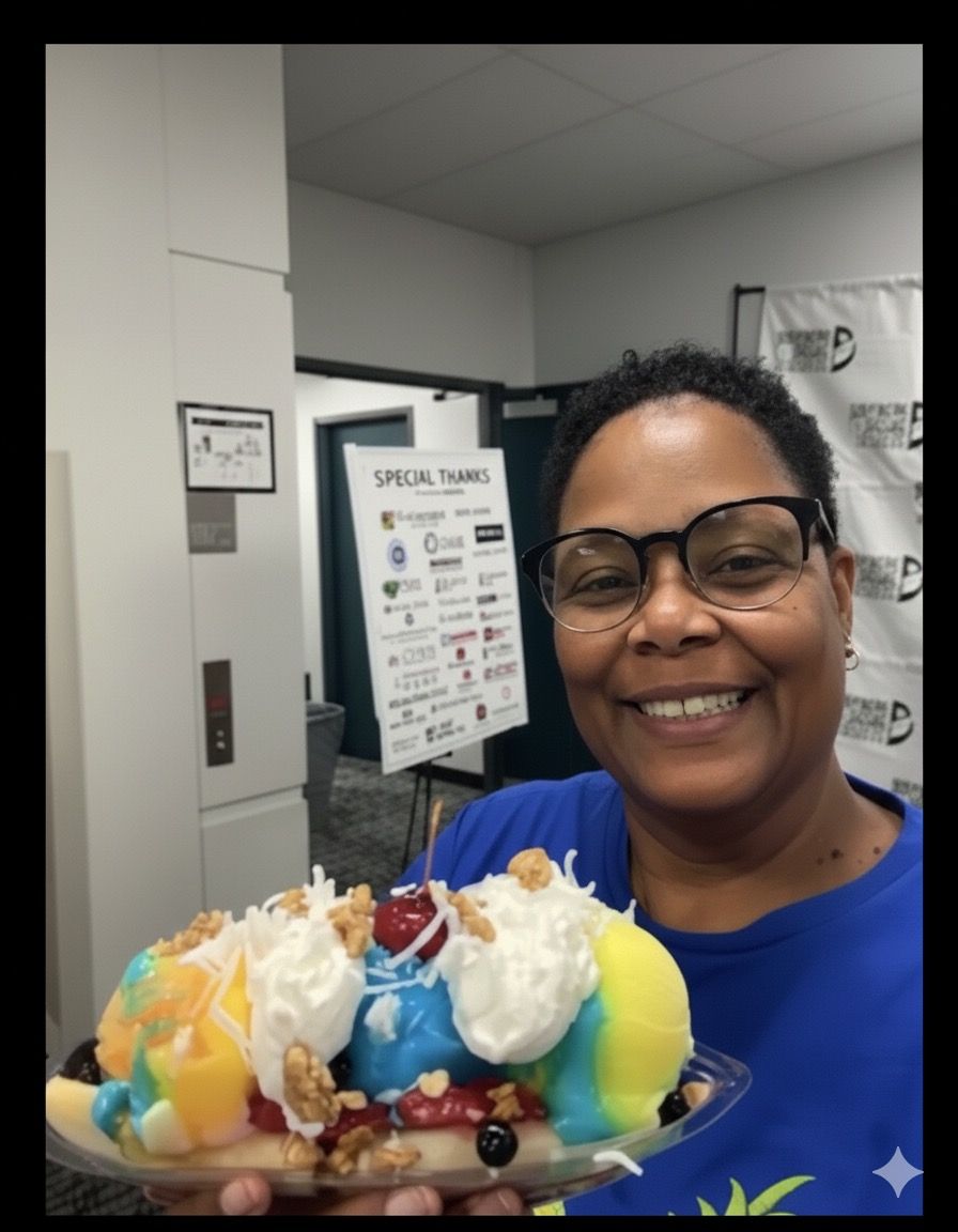 Woman holding a large banana split; smiling, inside a building with a “Special Thanks” sign.